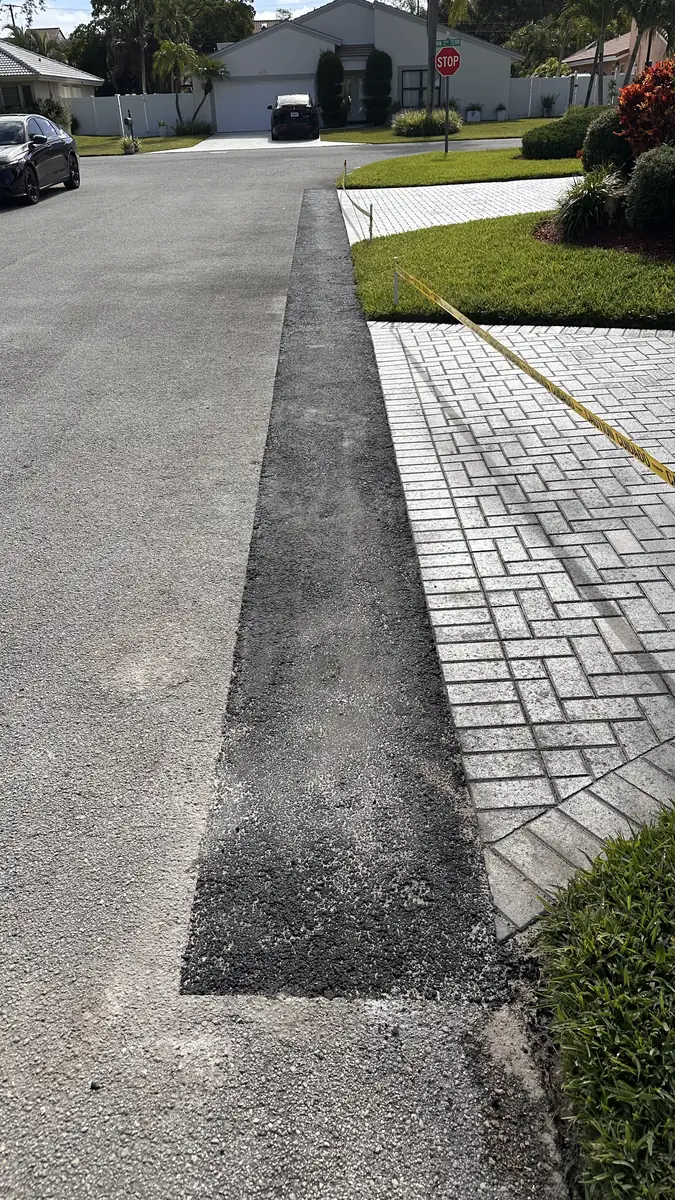 Straight completed asphalt repair line beside the paver driveway edge